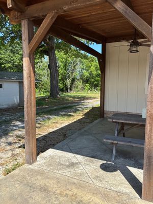 A covered porch or shelter structure with wooden beams and concrete flooring, showing the exterior condition of a