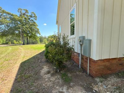 Exterior view of a mobile home foundation with landscaping, showing no visible repair work, drainage hardware, or