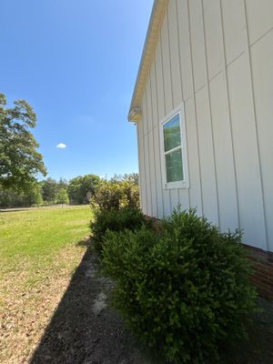 A residential foundation exterior showing a metal-sided house with a window, surrounding landscaping with shrubs and a