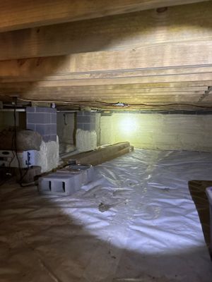 A crawl space showing plastic sheeting being installed on the floor as part of encapsulation work, with exposed wooden