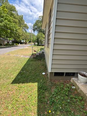 Exterior view of a house foundation and lawn with no visible repair work, drainage hardware, or active