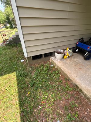 Exterior view of a house foundation with concrete pad and surrounding lawn, showing the pre-work condition with no