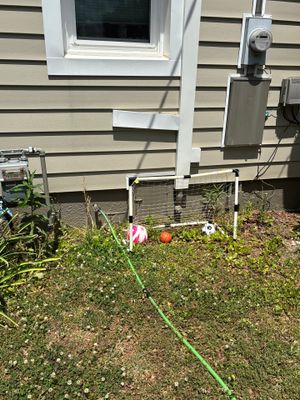 Exterior yard drainage installation in progress with a green drainage line laid across the lawn near the foundation of