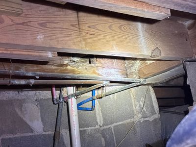 Interior crawlspace showing installed drainage pipe with blue and red fittings running along the foundation perimeter,
