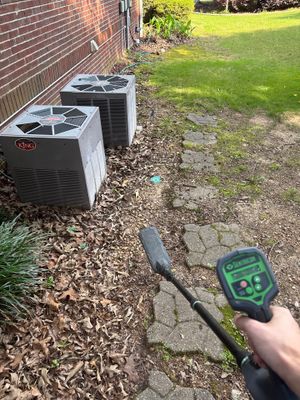An HVAC unit installation site with a technician using a moisture meter to assess soil conditions near exterior