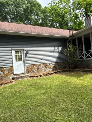 A residential home exterior with a white vinyl-sided addition, stone foundation visible, and a manicured lawn with no