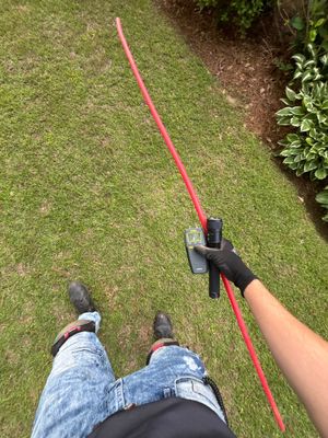 A technician is installing or measuring a red drainage pipe in a lawn, likely for exterior yard drainage