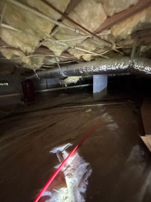 Interior crawlspace or basement with standing water, visible drainage piping, and what appears to be sump pump