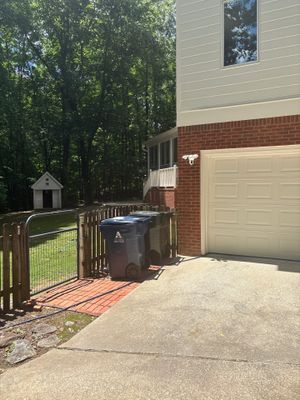 A residential home exterior showing a driveway, garage, wooden deck with gate, mailbox, and landscaped yard with