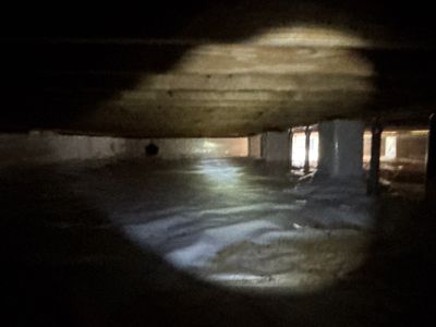 A dark, low-quality photo of a basement or crawlspace with visible water pooling on the floor and interior drainage