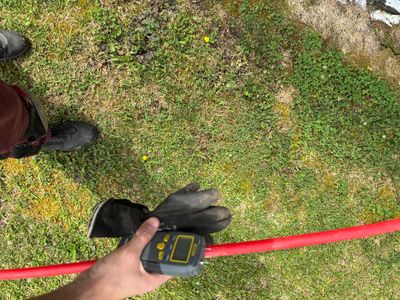 A worker uses a measuring tape to measure yard drainage layout or spacing on a grassy lawn with soil