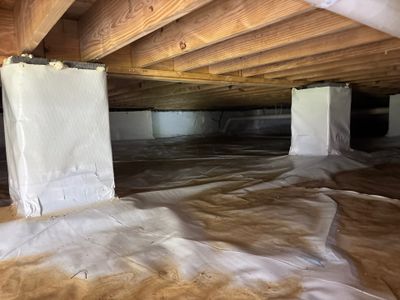 A crawl space with white encapsulation liner being installed on walls and brown water/moisture visible on the floor,
