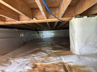 A crawl space is being encapsulated with white plastic sheeting installed on the floor and walls, with interior
