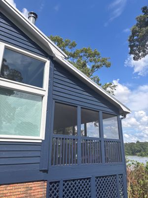 A residential house exterior with a blue-gray deck and lattice foundation skirt overlooking a waterfront property,