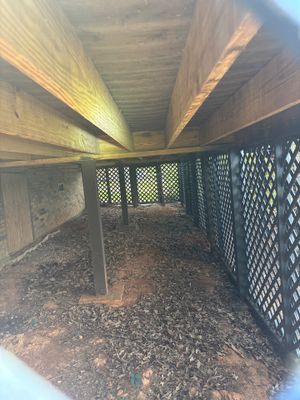Interior view of an empty crawl space with wooden beams, posts, and lattice ventilation panels showing the pre-work