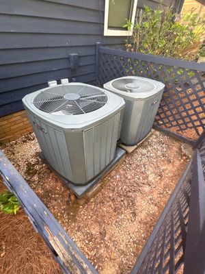 Two HVAC units installed on a finished concrete pad in a residential yard with completed landscaping and