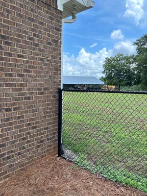 Exterior view of a brick building with a chainlink fence and grassy yard showing no visible foundation repair or