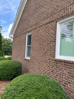 Exterior view of a brick residential foundation with landscaping, showing no visible repair work or installed drainage