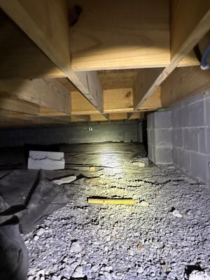 An active foundation repair job showing exposed crawlspace with gravel base material, interior drainage installation