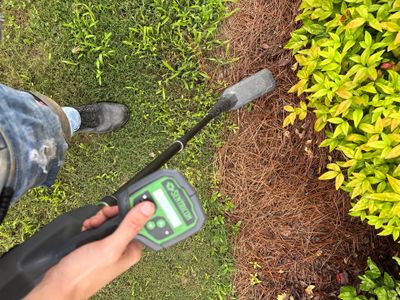 A technician uses a moisture meter to assess soil and drainage conditions around foundation perimeter, with visible