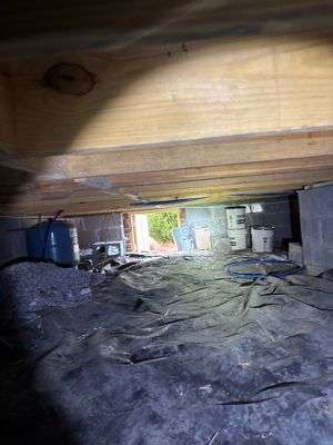 A crawl space with plastic sheeting laid on the ground floor during an ongoing encapsulation project, with wooden beam
