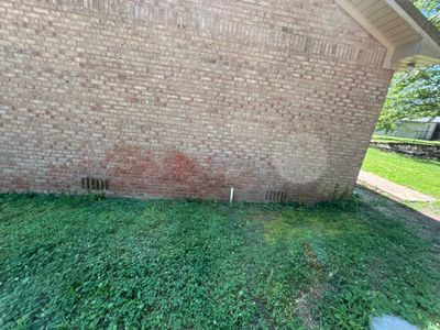 Exterior view of a brick foundation wall with adjacent lawn and minimal visible site conditions, showing no active