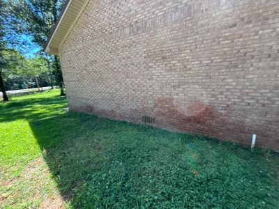 A clean exterior view of a brick foundation wall with adjacent lawn and landscaping, showing no visible repair work,