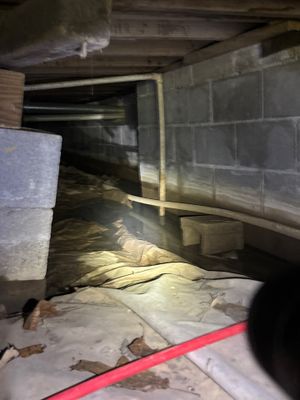 Crawlspace interior showing active installation of drainage channel and white encapsulation vapor barrier along the