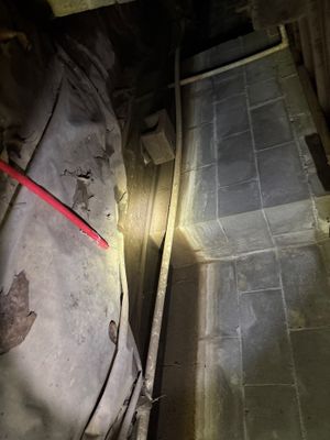 A dimly-lit interior crawlspace or basement showing exposed foundation wall, floor, and what appears to be interior