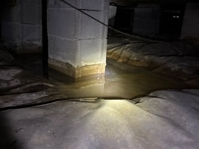 An interior drainage system with what appears to be a sump basin or collection pit is visible in a dimly lit crawl