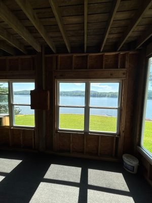 Interior view of a wooden structure with large windows overlooking a waterfront landscape, showing no visible
