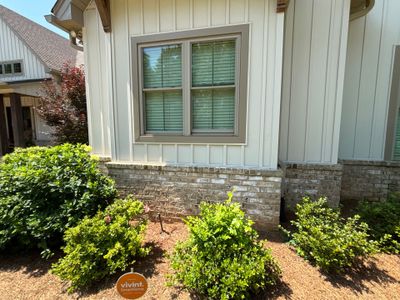 A clean exterior view of a modern house foundation with white siding, stone veneer base, and landscaped shrubs showing