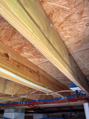 Installation of wooden beams and blue steel I-beams under a ceiling/foundation structure during active repair