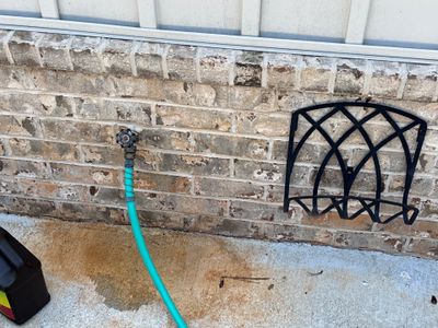 Exterior foundation area with a green drainage hose and black plastic catch basin/drain box installed against a brick
