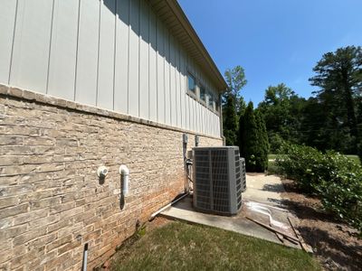 Completed exterior foundation work showing a newly installed HVAC unit on a concrete pad against a brick and