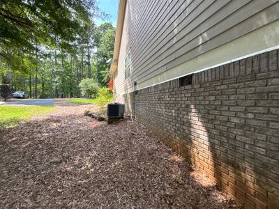 Exterior view of a house foundation with brick and siding showing the ground level and lawn area with no visible repair