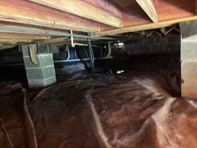 A crawlspace showing black encapsulation membrane being installed over the dirt floor with interior drainage