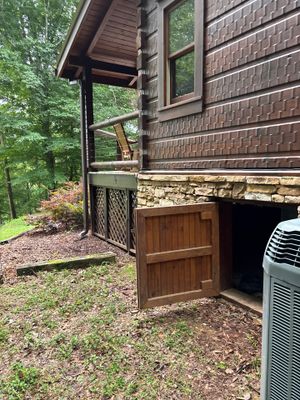 Exterior view of a residential cabin/home with wood siding, stone foundation detail, wooden deck door, and landscaped