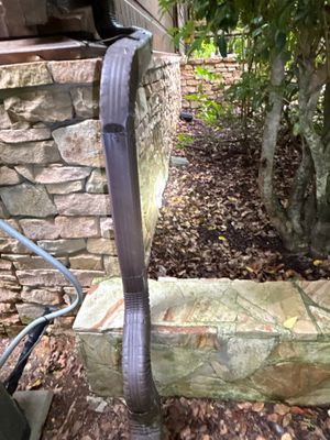 Exterior yard drainage installation in progress with a blue drainage pipe positioned along a stone foundation wall and