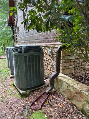 An exterior HVAC unit is installed next to a stone foundation with a yard-drainage system featuring a discharge line