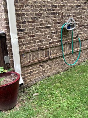 Exterior yard drainage system installation in progress with a green drain line and catch basin positioned against a