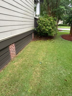 Exterior view of a house foundation and yard with green lawn, showing no visible repair work or drainage hardware