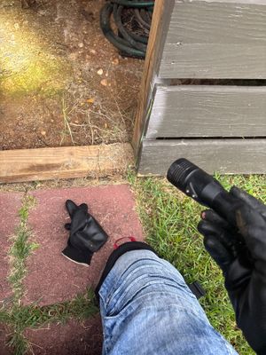 A technician in work gloves is installing or inspecting a black drainage pipe or conduit in an exterior yard area with