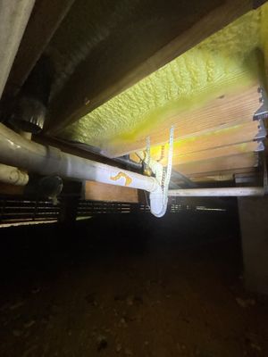 Interior crawl space or basement showing drainage pipe installation under a beam with yellow insulation visible
