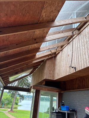 A screened porch or sunroom with exposed wooden ceiling beams, skylights, and a view of a lakeside property with no