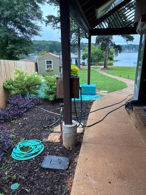 Exterior yard drainage system installation in progress with a coiled green discharge hose and drainage basin staged on