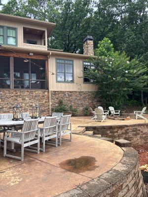 A residential backyard showing an outdoor patio area with brick foundation, seating, and landscaping with no visible
