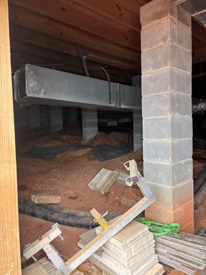 Active crawlspace excavation and drainage installation with exposed foundation, drainage pipe staging, and void-fill