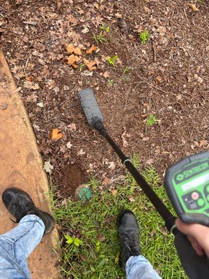 An exterior yard drainage installation in progress with a drain pipe or conduit being positioned in a lawn area with