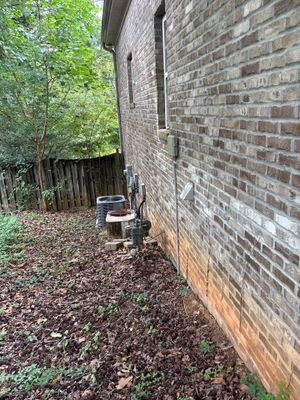 Exterior view of a brick foundation wall with mulched ground and natural vegetation, showing no visible repair work or